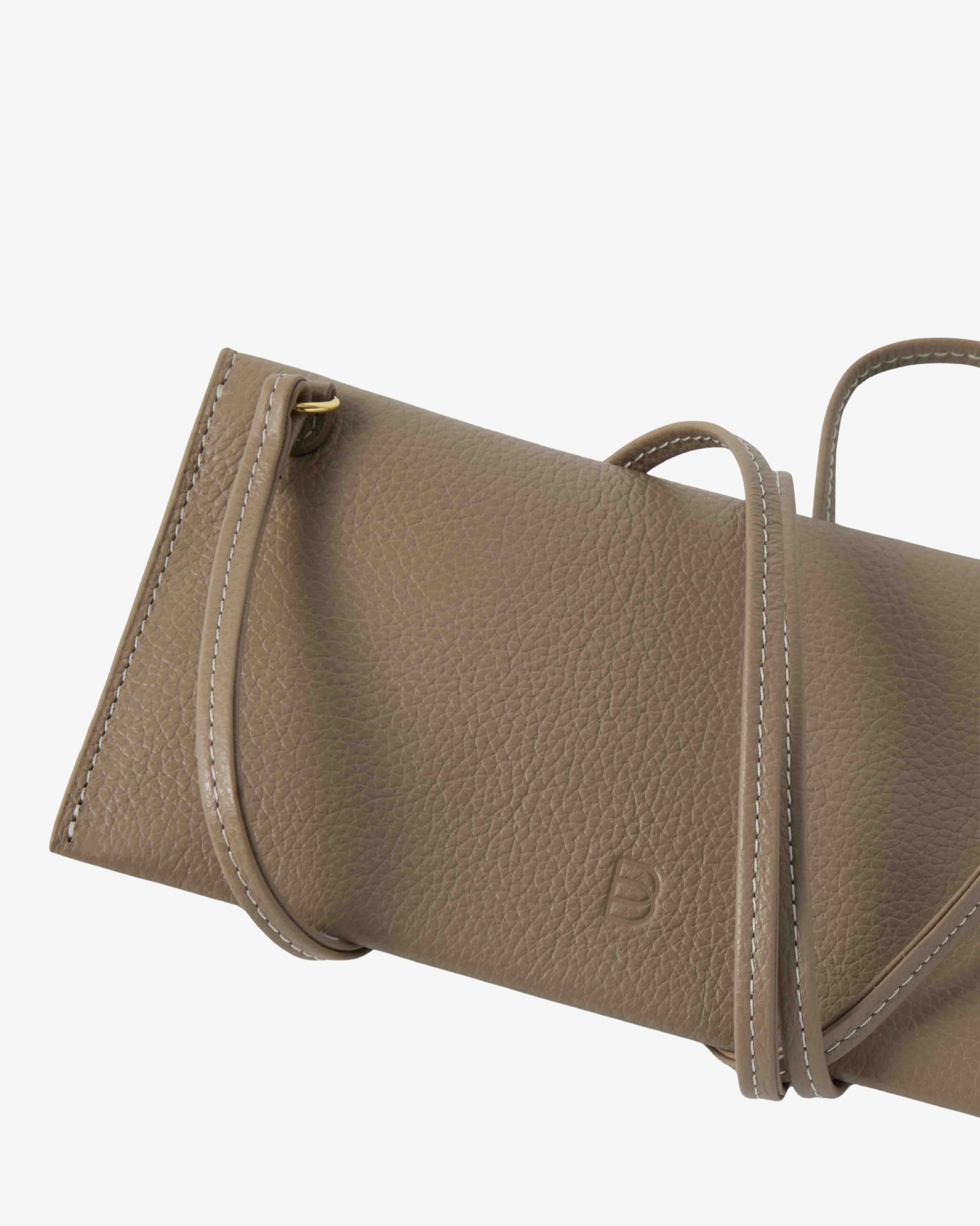 A close-up of a taupe pebbled leather handbag showing the side profile, top handle, and a small debossed logo on a light gray background.