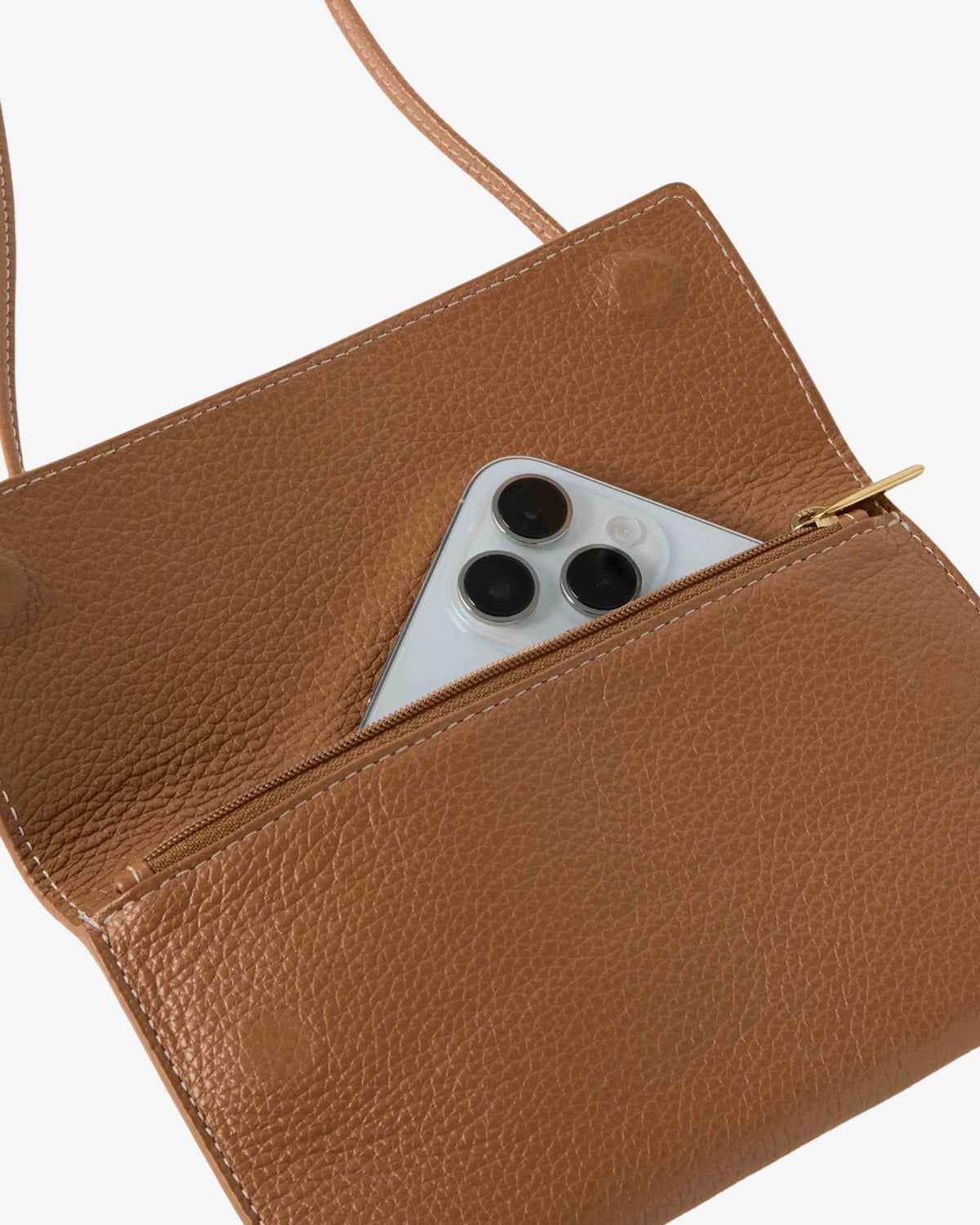 A close-up of a tan pebbled leather crossbody bag with a zippered pocket containing a silver smartphone, set against a plain white background.