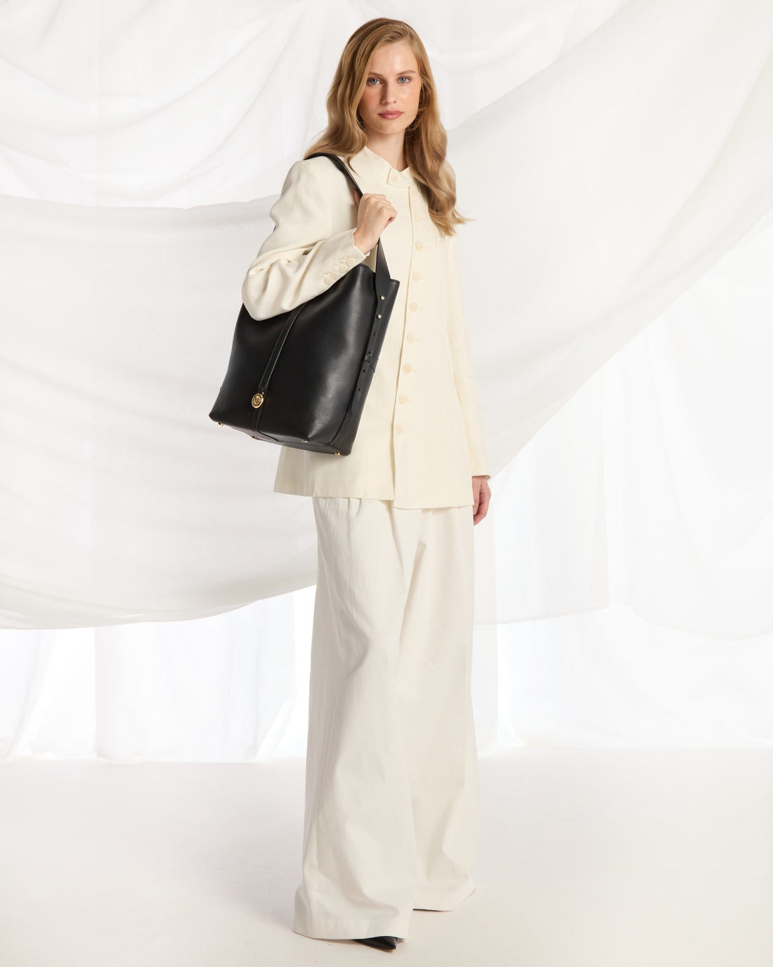 A black leather bucket bag with a single shoulder strap and gold-tone hardware, shown against a plain light gray background.