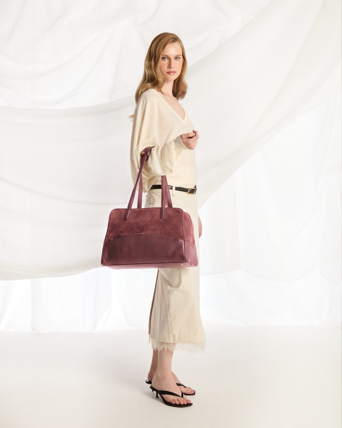 A burgundy leather duffel bag with dual top handles and a front zippered pocket, shown against a plain white background.