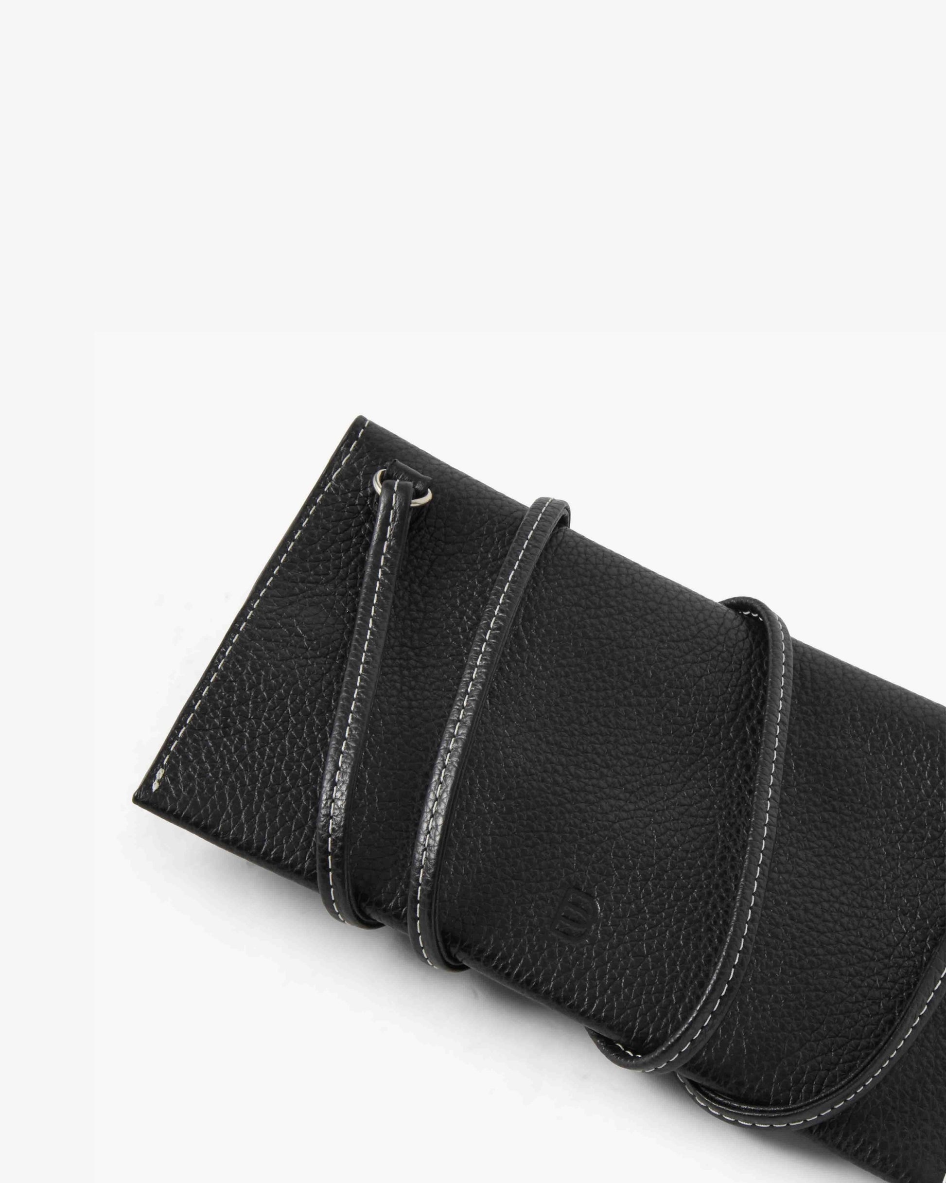 A close-up of a black pebbled leather accessory, likely a pouch or sleeve, featuring a strap with white contrast stitching and a small embossed logo on a clean white background.