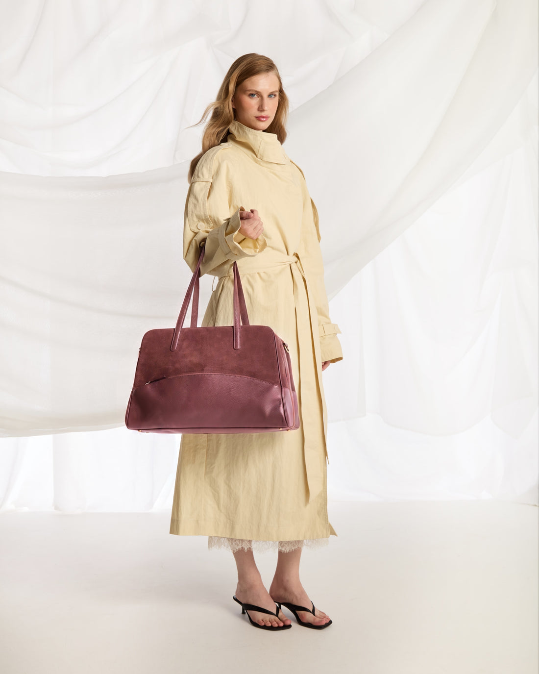 A burgundy leather handbag with dual top handles and a curved front pocket, photographed against a clean white background.