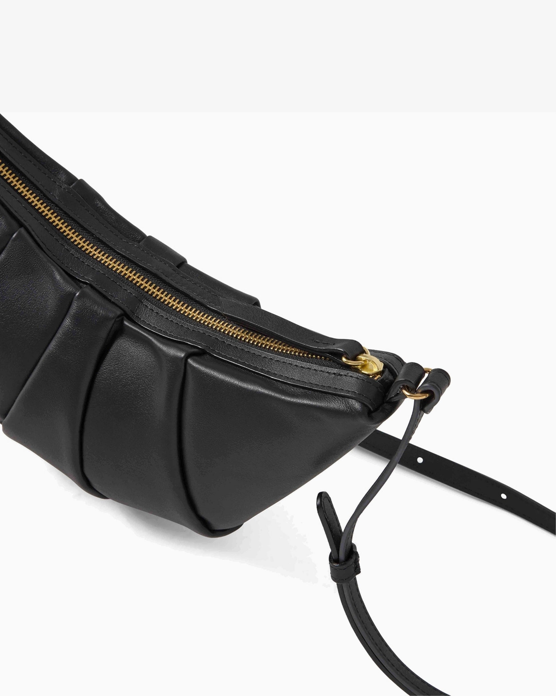 A close-up of a black leather crossbody bag with pleated detailing, a gold zipper, and a black adjustable strap on a clean white background.