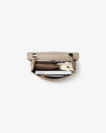 A beige leather zippered briefcase shown open from a top-down view, revealing a silver metal lunchbox, a black circular item, and other small accessories inside, set against a plain white background.
