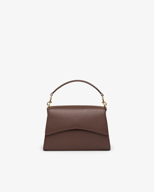 A brown leather top-handle handbag with a curved flap front and gold-tone hardware, centered on a plain light gray background.