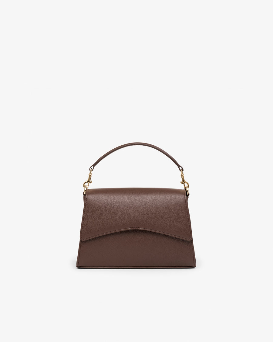 A brown leather top-handle handbag with a curved flap front and gold-tone hardware, centered on a plain light gray background.
