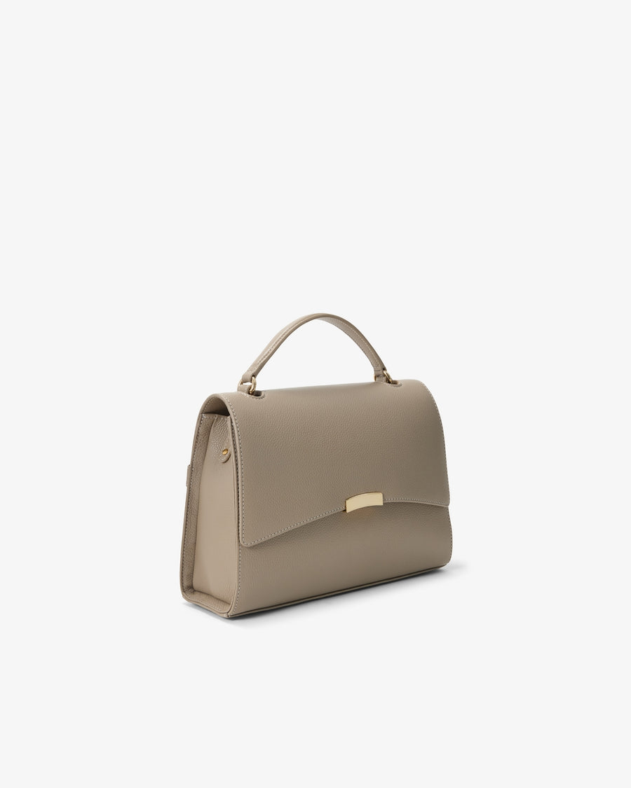 A structured taupe handbag with a top handle and a small gold-tone metal accent on the front, shown against a plain white background.