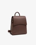 A brown pebbled leather backpack with a top handle and a front flap, shown from the side on a light gray background.