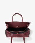 A top-down view of a burgundy leather tote bag with a black interior lining and gold-tone hardware, set against a plain white background.