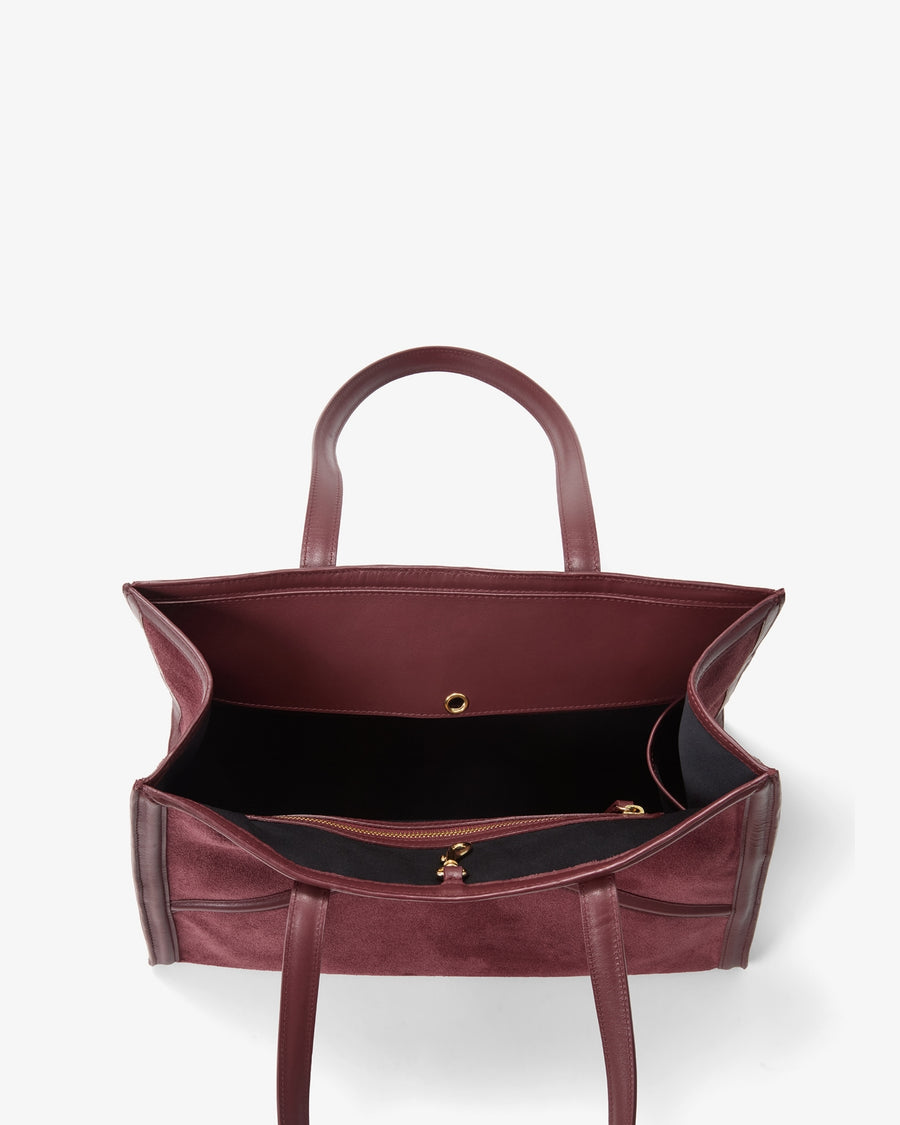 A top-down view of a burgundy leather tote bag with a black interior lining and gold-tone hardware, set against a plain white background.