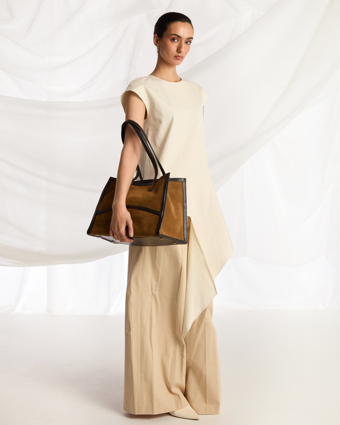 A structured tote bag made of brown suede with black leather trim and handles, shown on a plain light gray background.