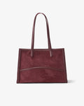 A dark burgundy suede tote bag with smooth leather handles and trim, shown against a plain light gray background.