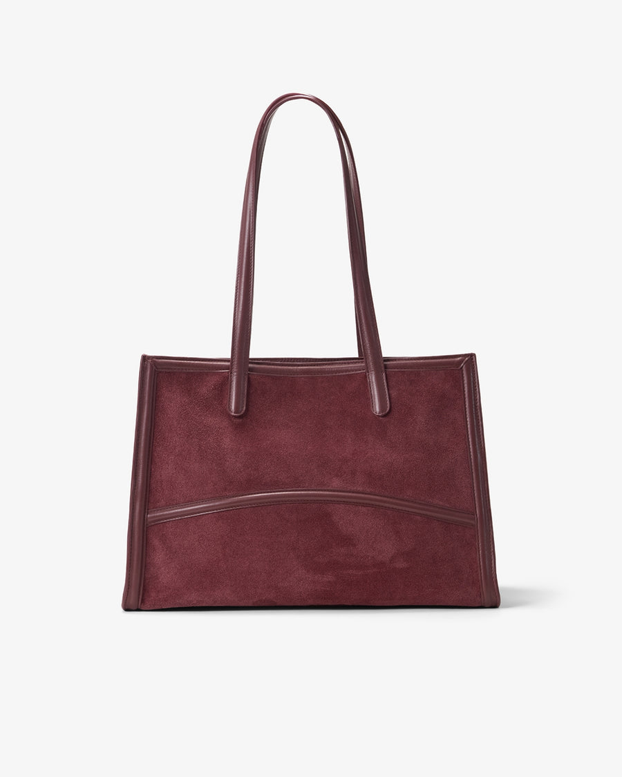 A dark burgundy suede tote bag with smooth leather handles and trim, shown against a plain light gray background.