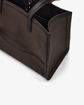 Close-up of a dark brown pebbled leather tote bag with black trim and handles, showing the interior zipper and corner details on a light gray background.