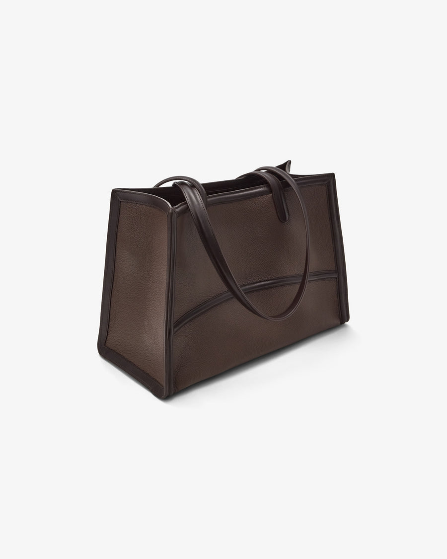 A dark brown leather tote bag with dual top handles, shown from a three-quarters perspective on a clean, light off-white background.