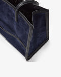 Close-up of a navy blue suede tote bag with black leather trim and handles, shown on a clean white background.