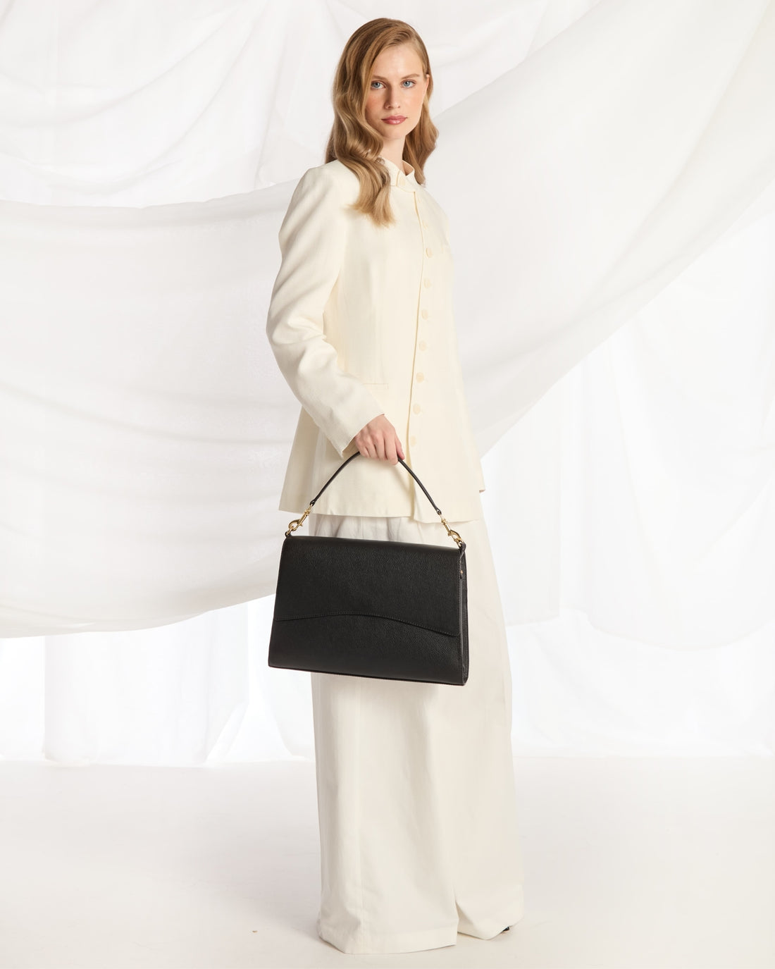 A black leather shoulder bag with a curved flap and gold-tone hardware, shown against a plain white background.