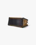 A leather bag shown from a bottom angle on a clean white background, featuring a dark brown leather panel and tan suede-like side panels with metal feet.