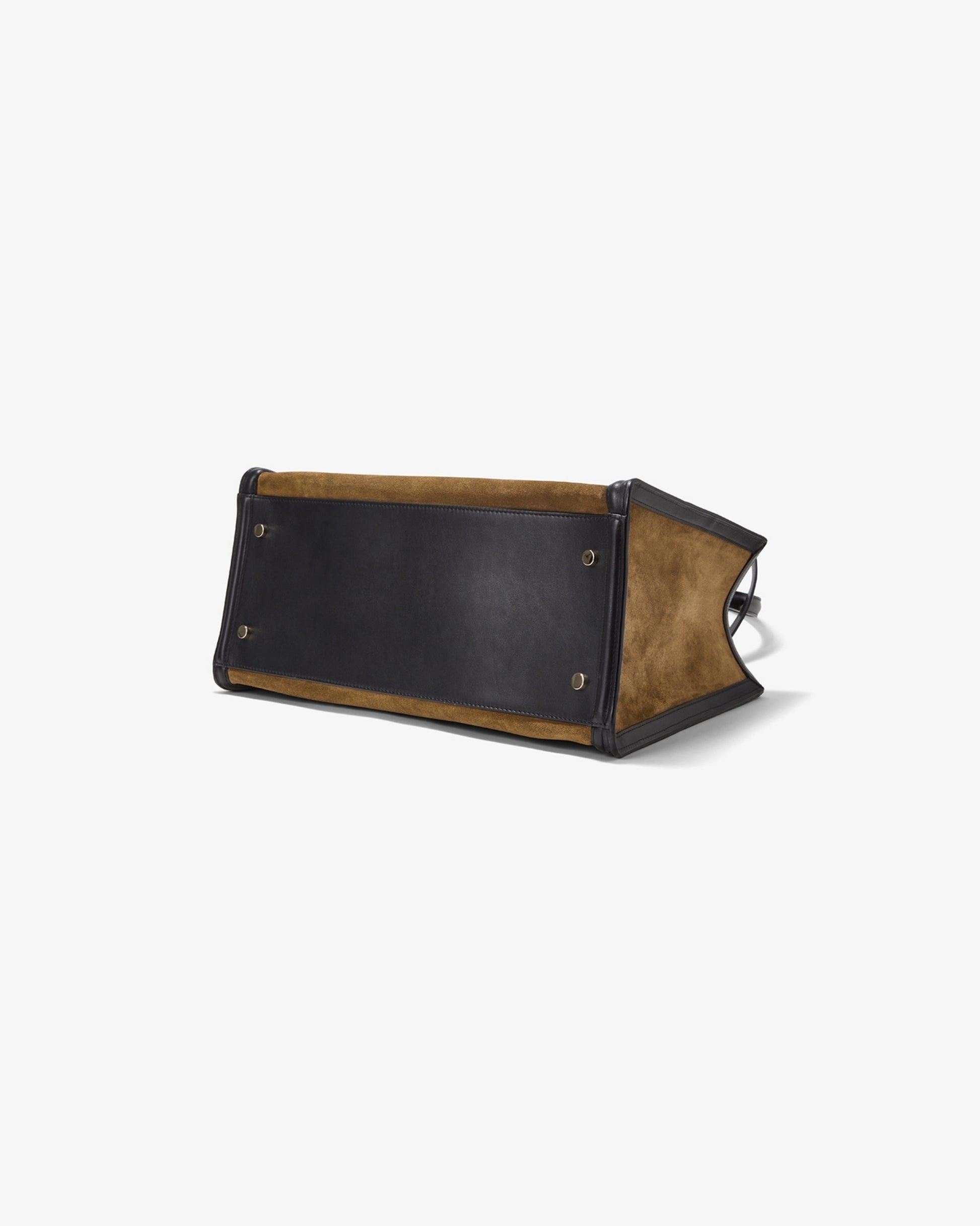 A leather bag shown from a bottom angle on a clean white background, featuring a dark brown leather panel and tan suede-like side panels with metal feet.