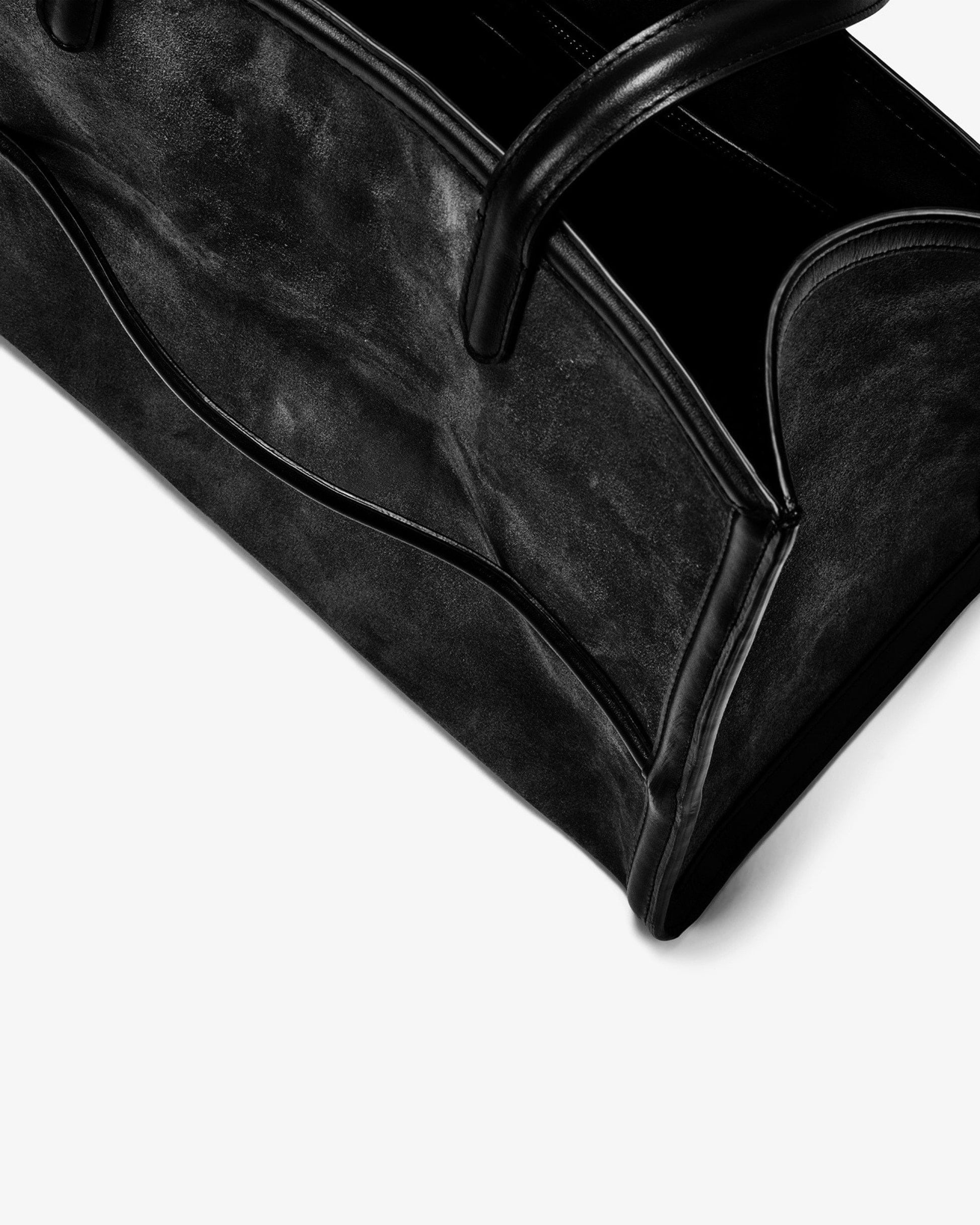Close-up of a black leather or faux-leather handbag corner with curved top handles and a soft shadow on a white background.