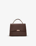 A structured dark brown leather handbag with a top handle and a small gold-tone metal accent on the front flap, shown against a plain light gray background.