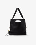A black leather shoulder bag with a top handle, a rectangular cutout detail on the front, and a small hanging tassel charm, shown against a plain light gray background.