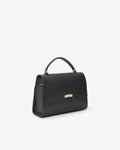 A black leather top-handle handbag with a small gold-tone metal accent on the front, shown from a three-quarters angle against a plain white background.