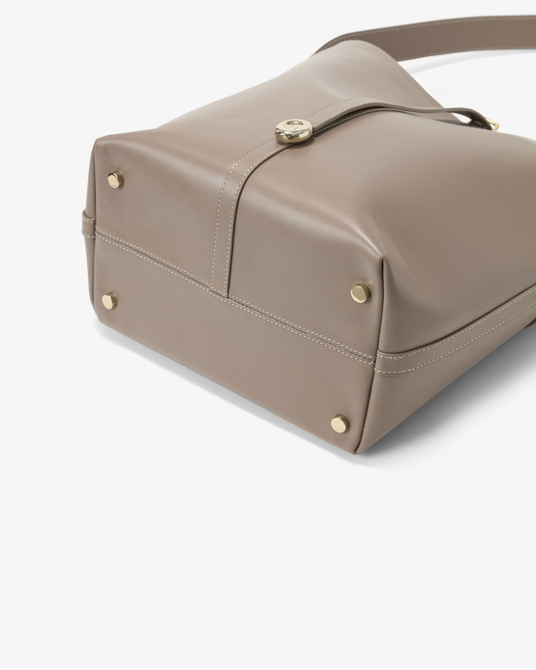 Close-up of a taupe leather shoulder bag showing the bottom corner with gold-tone rivets and a strap closure, on a clean white background.