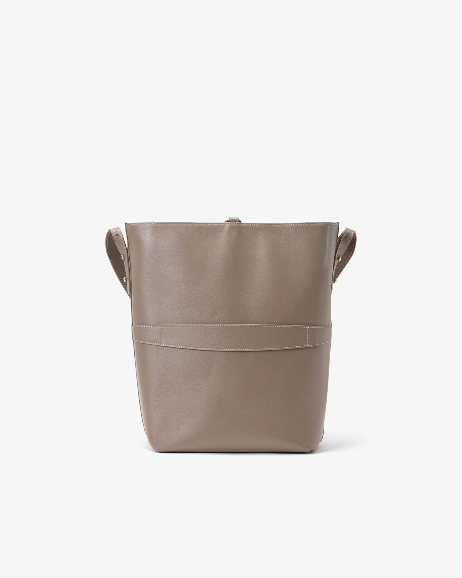 A taupe leather bucket bag with integrated side handles and a horizontal luggage strap, shown from the back against a plain white background.