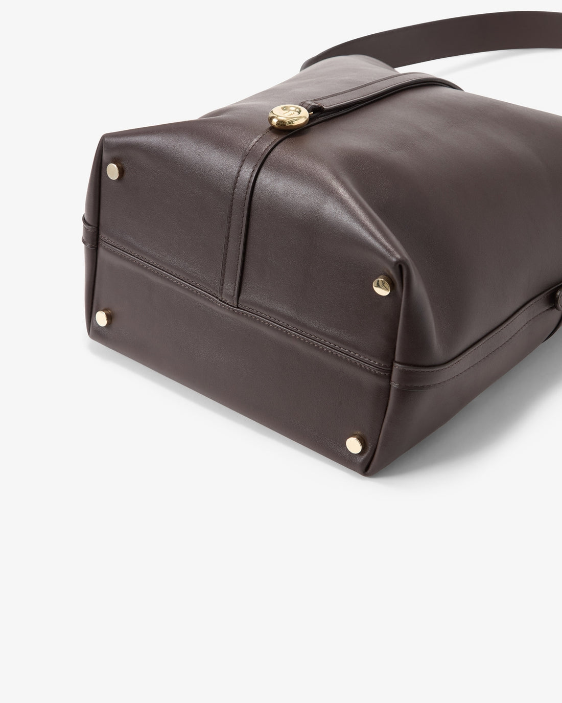 A close-up of a dark brown leather shoulder bag showing the bottom corner, gold-tone hardware, and strap attachment on a light gray background.