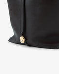 Close-up of a black leather bag with a gold-tone circular medallion featuring a logotype.