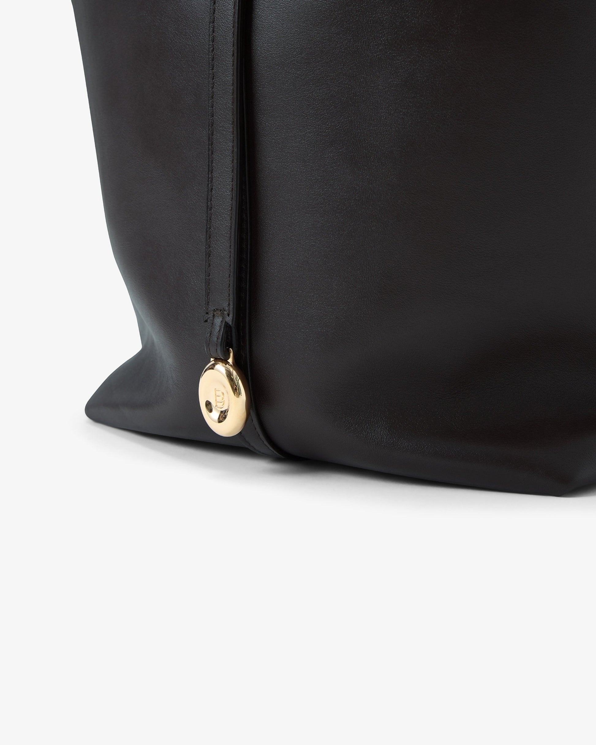 Close-up of a black leather bag with a gold-tone circular medallion featuring a logotype.