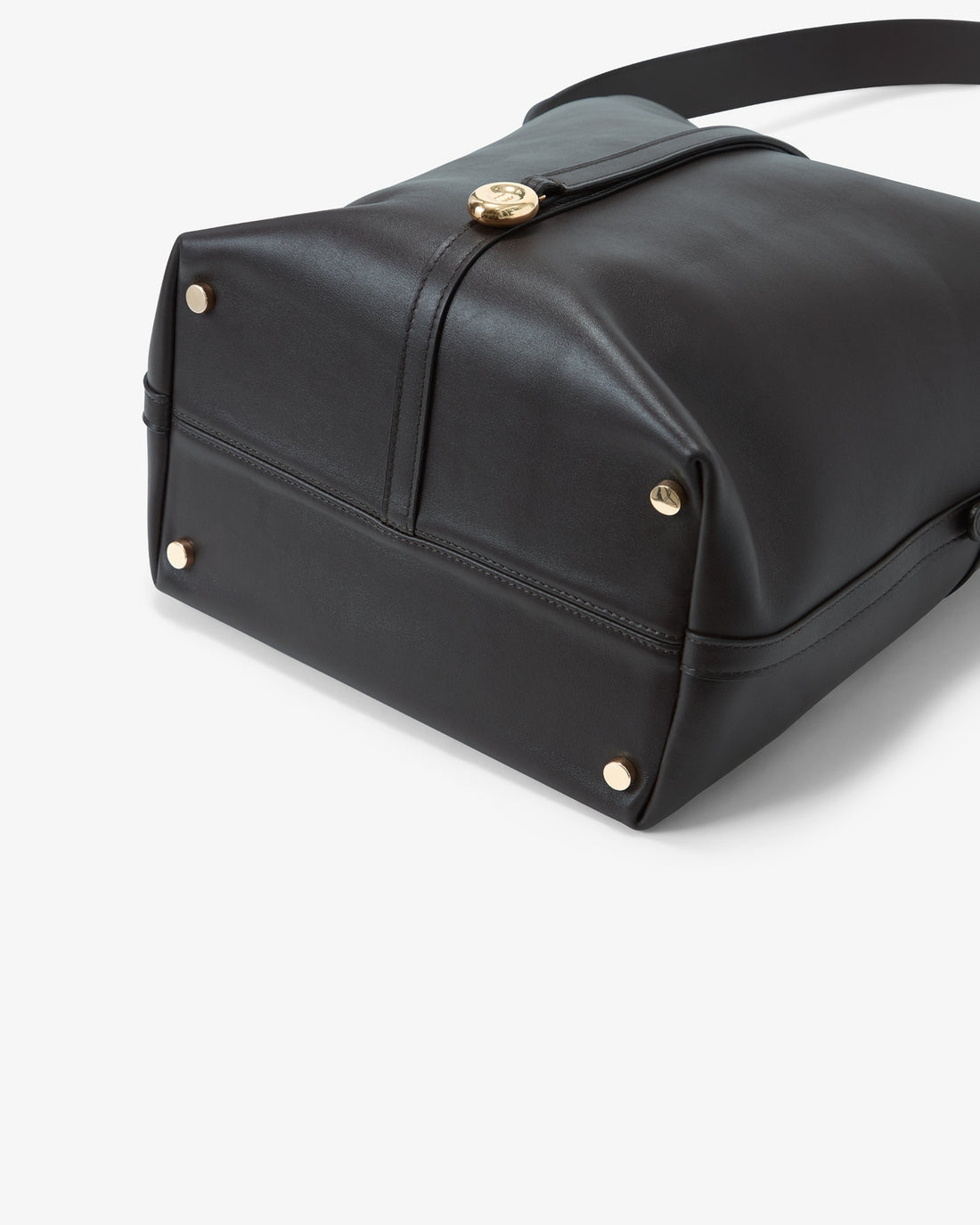 Close-up of a black leather shoulder bag showing the bottom corner with gold-tone rivets and a clasp closure, on a light gray background.