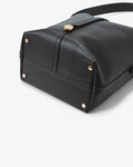 Close-up of a black leather shoulder bag showing the bottom corner with gold-tone rivets and a clasp closure, on a light gray background.