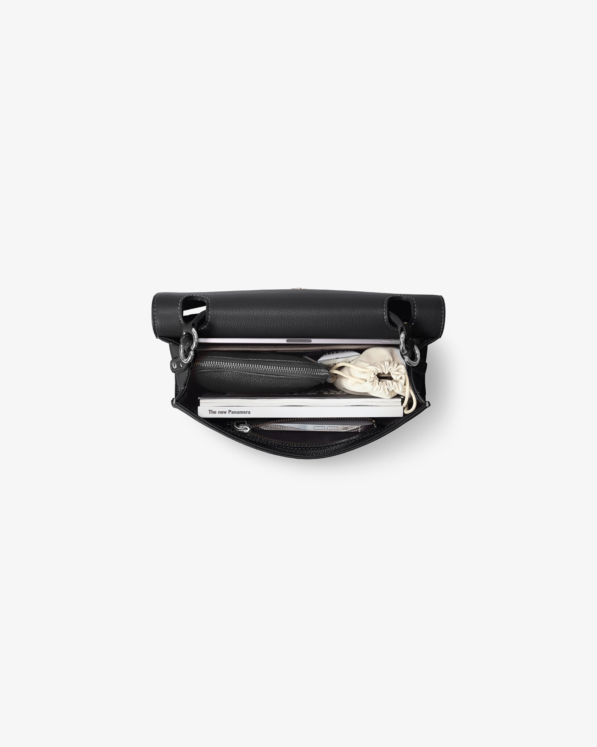 A black leather bag shown open from a top-down view, containing a black wallet, sunglasses, and a white scarf, set against a plain light gray background.