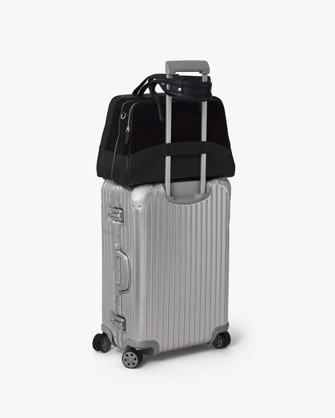 A silver hard-shell spinner suitcase with a telescoping handle extended, carrying a black duffel bag on top, photographed on a clean light gray studio background.