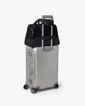 A silver hard-shell spinner suitcase with a telescoping handle extended, carrying a black duffel bag on top, photographed on a clean light gray studio background.