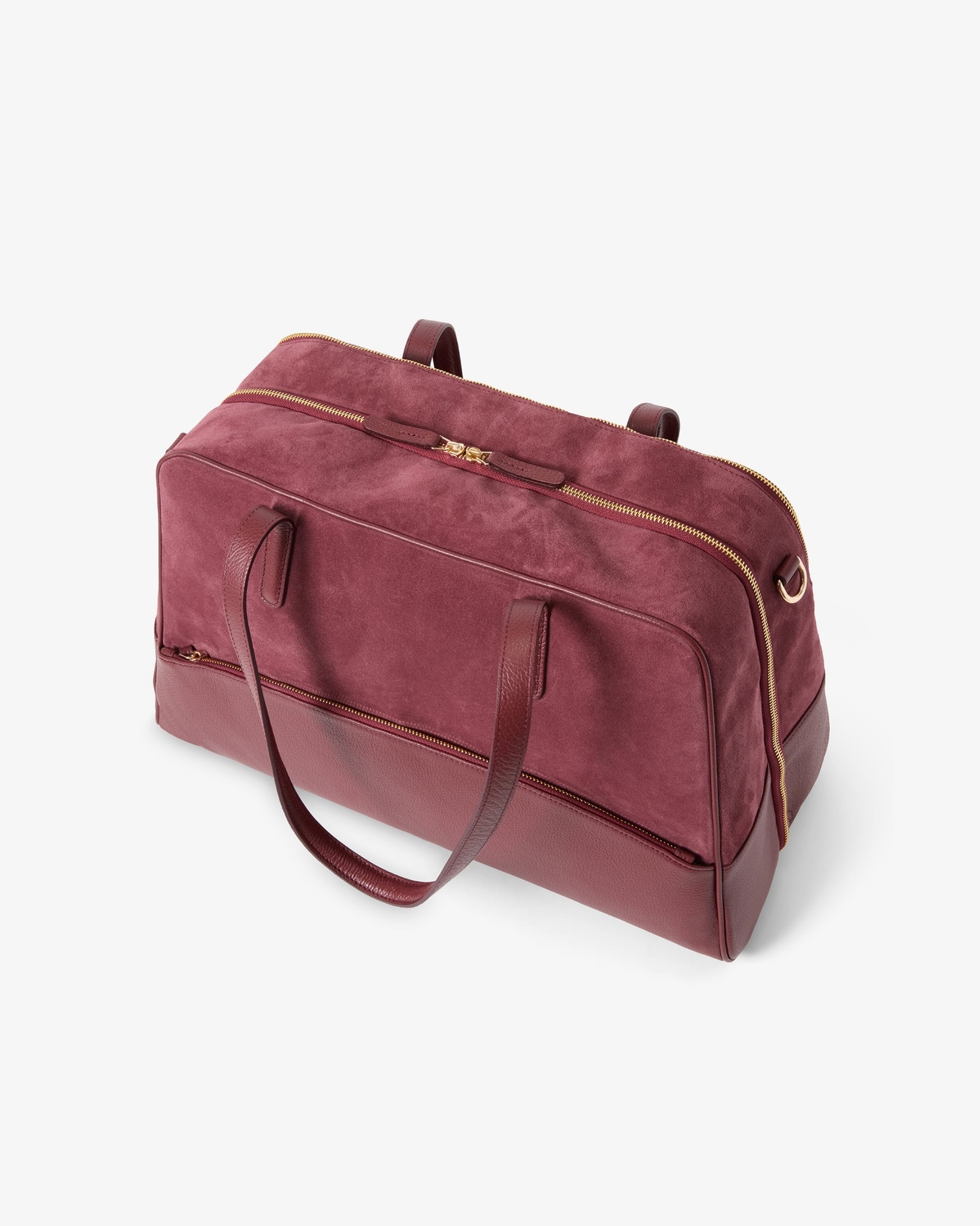 A burgundy suede duffel bag with dark maroon leather handles and gold-tone zipper accents, photographed on a clean white background.