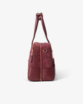 A burgundy leather duffel bag with gold-tone hardware, shown from the side on a clean white background.