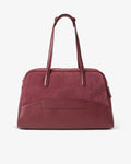 A burgundy leather and suede duffel bag with dual top handles and gold-tone hardware as well as a luggage strap, photographed against a clean white background.