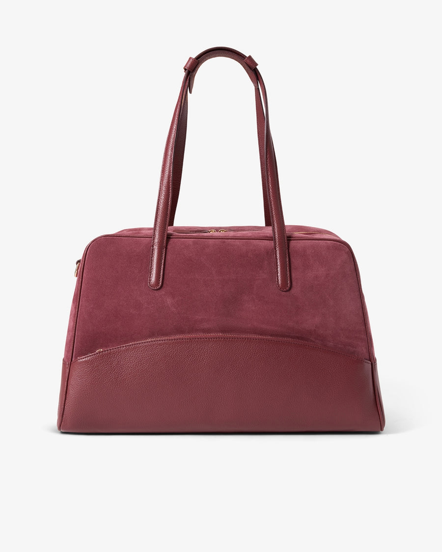 A burgundy leather handbag with dual top handles and a curved front pocket, photographed against a clean white background.