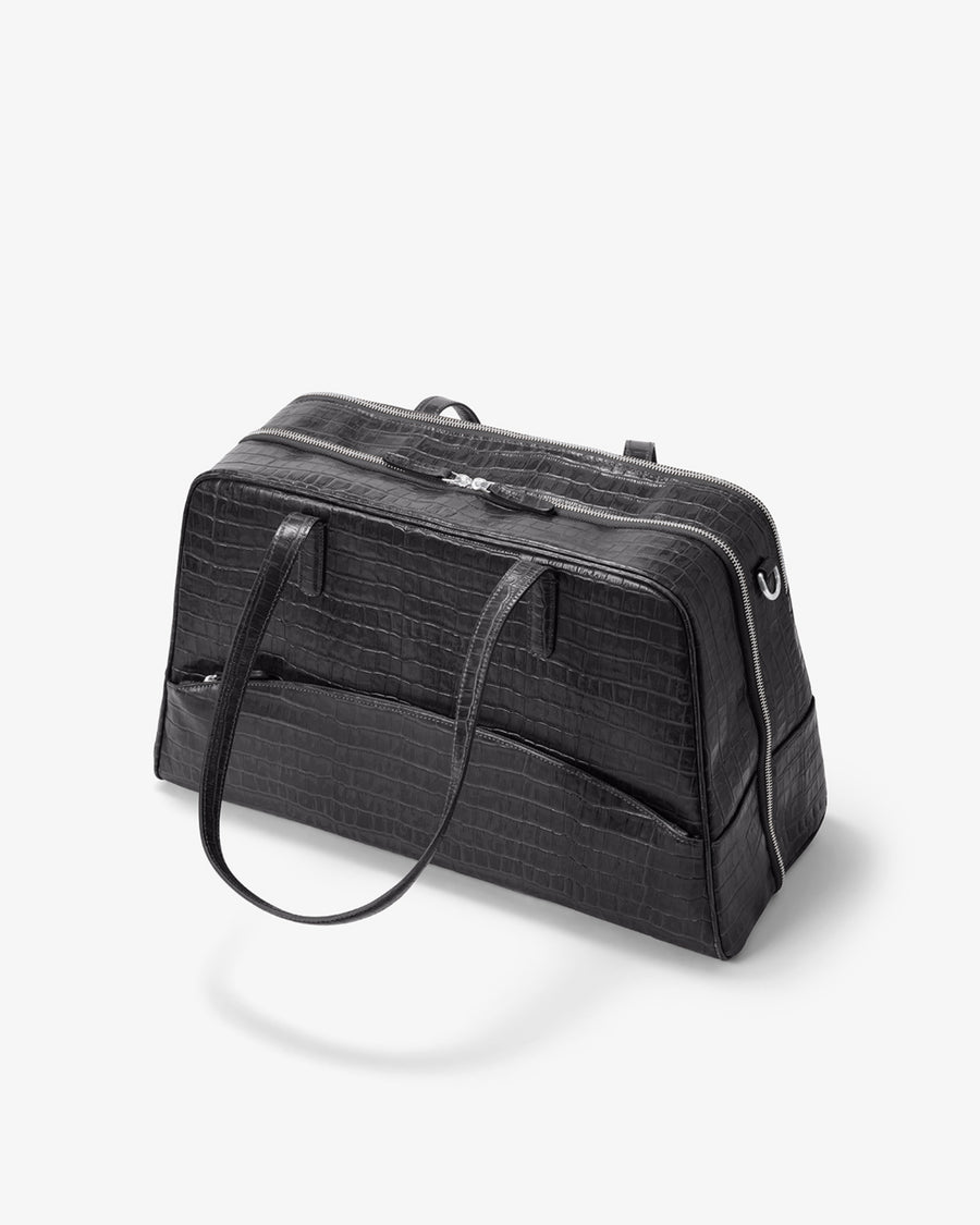 A black crocodile-embossed leather duffel bag with dual top handles and a zippered main compartment, shown on a light gray background.