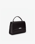 A black leather top-handle handbag with a silver-tone metal accent on the front flap, shown from a three-quarter angle against a plain white background.