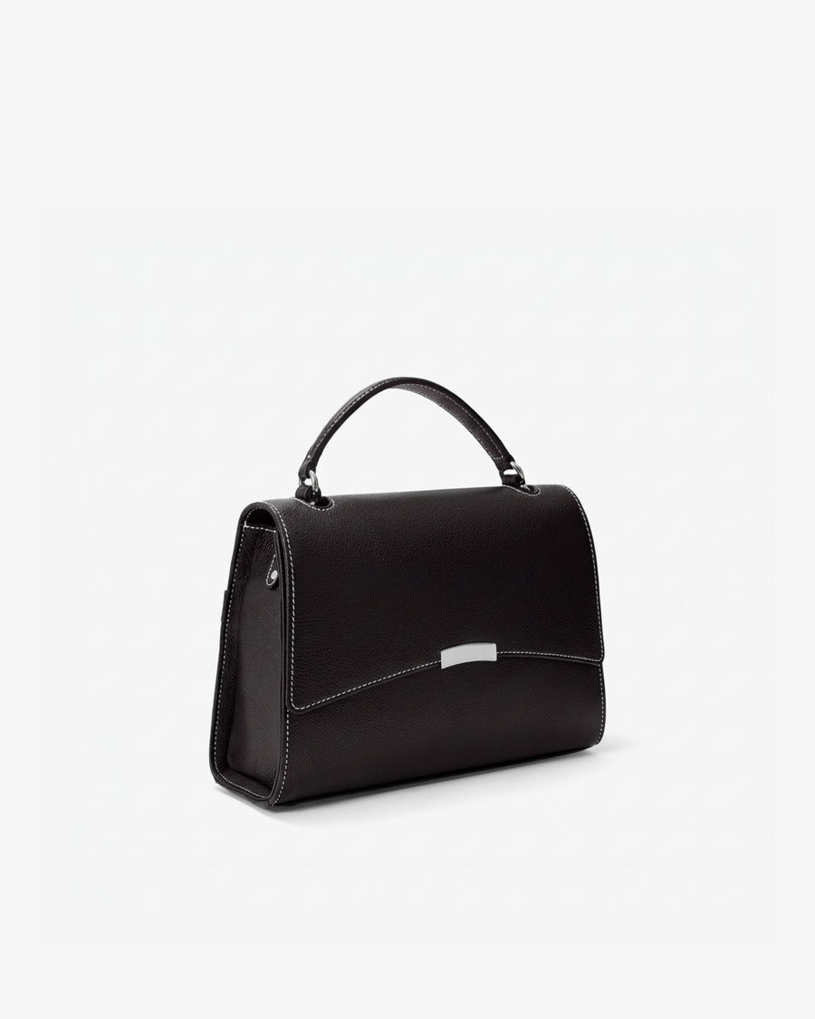 A black leather top-handle handbag with a silver-tone metal accent on the front flap, shown from a three-quarter angle against a plain white background.