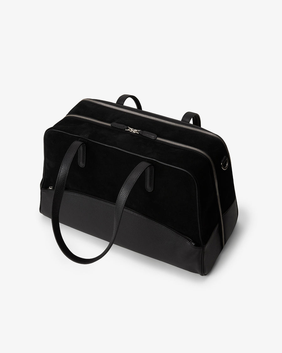 A black duffel bag made of leather and suede, with dual top handles and a shoulder strap, photographed on a clean white background.