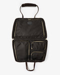 An open black nylon bag with multiple interior pockets, gold-tone zippers, and dark brown leather handles, shown against a light gray background.