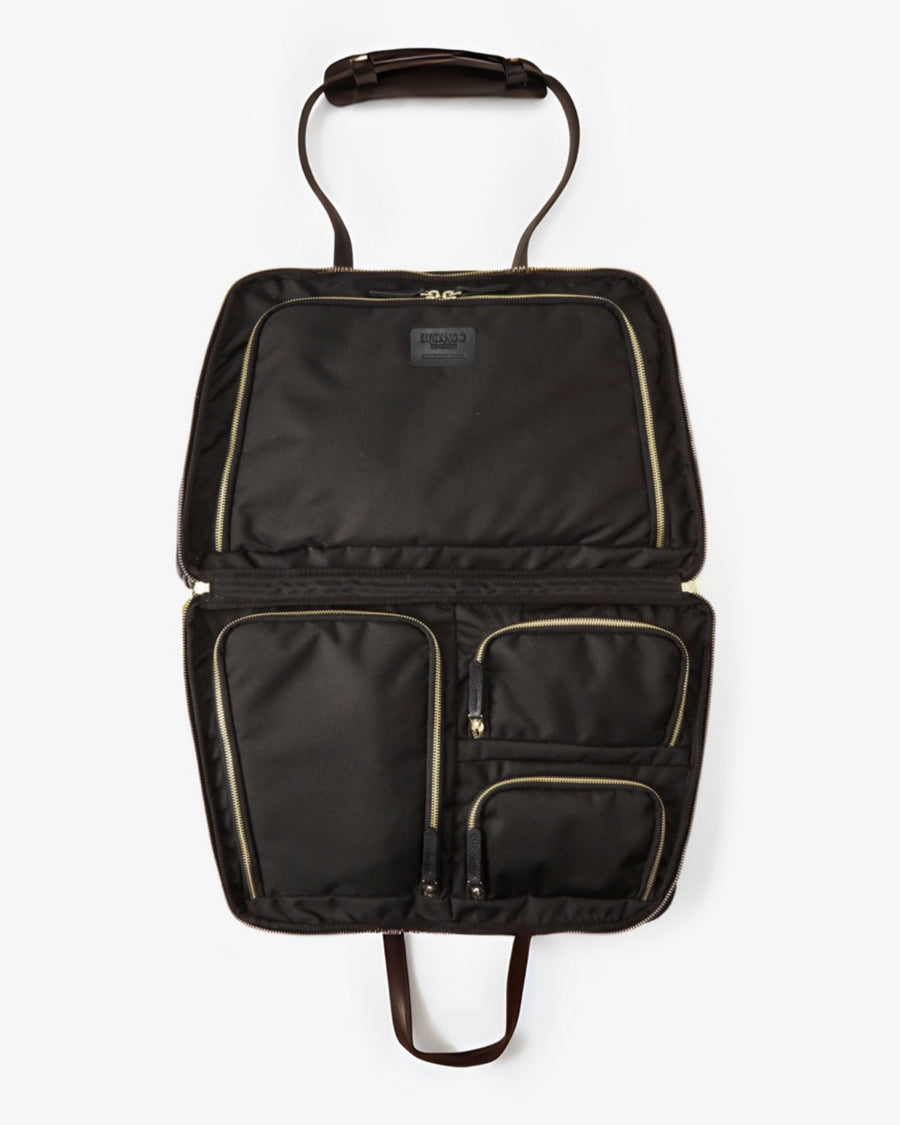 An open black nylon bag with multiple interior pockets, gold-tone zippers, and dark brown leather handles, shown against a light gray background.