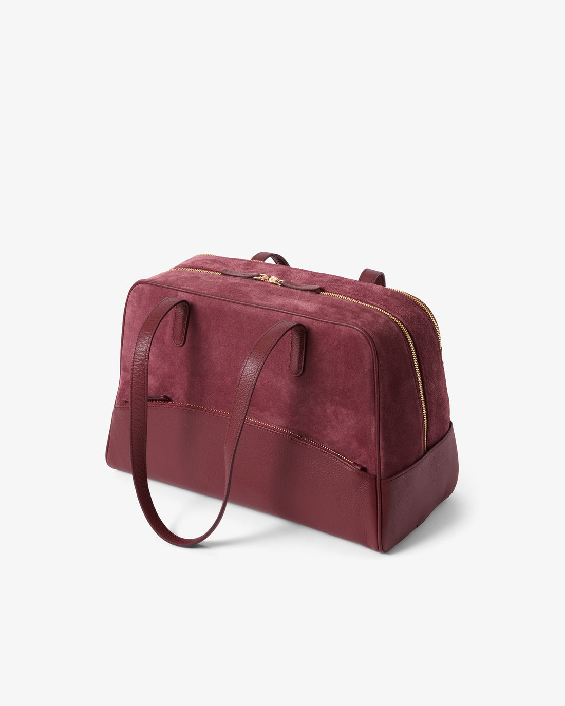 A burgundy suede and leather duffel bag with gold-tone hardware, shown from a three-quarter angle on a light gray background.
