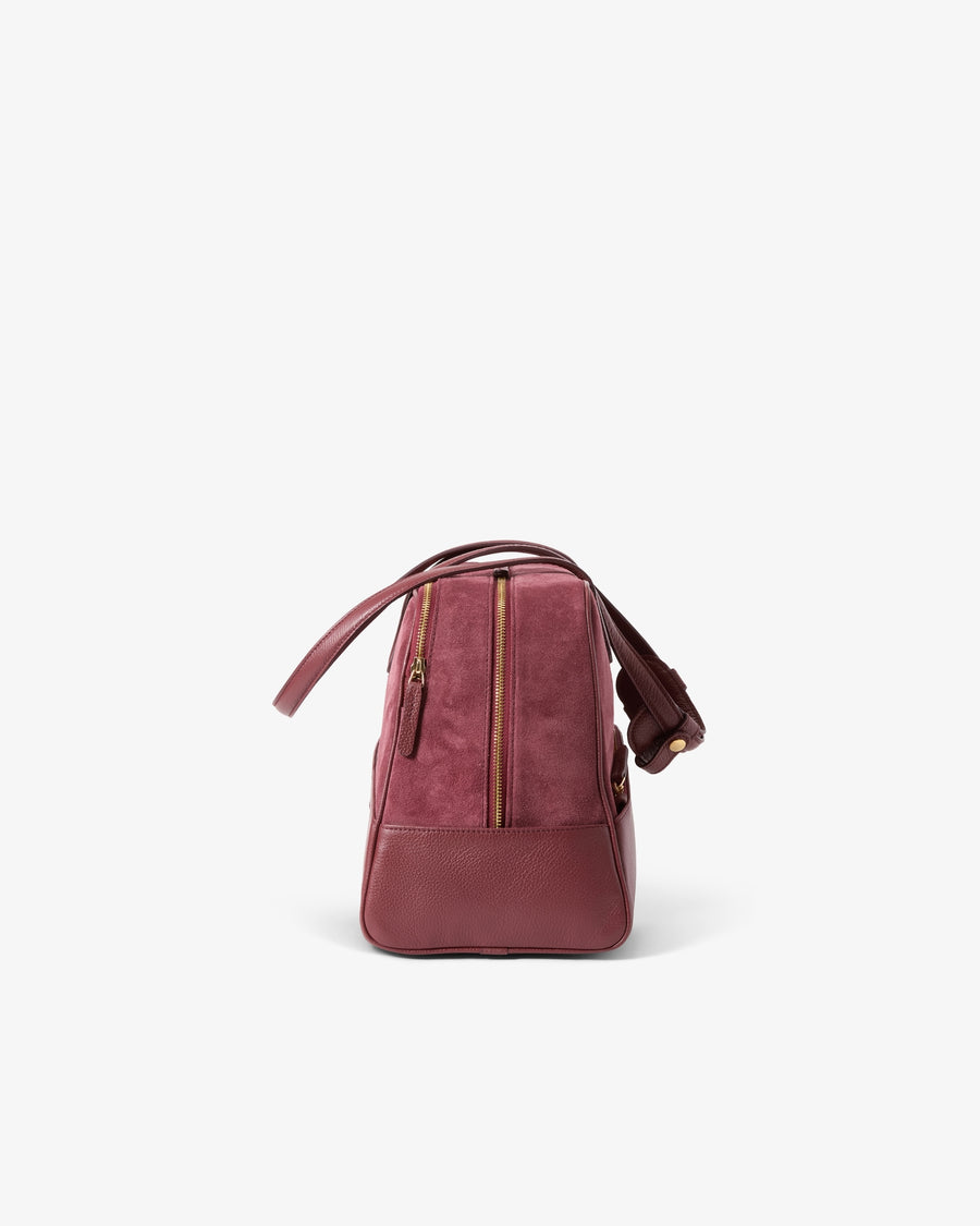 A burgundy leather bag with gold-tone zippers and a matching shoulder strap, shown from the back against a clean white background.