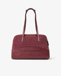 A burgundy leather handbag with dual top handles and a front slip pocket, as well as a luggage strap, photographed against a clean white background.